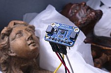 Elektronisches Messgerät im Vordergrund. Im Hintergrund liegen zwei hölzernen Figuren