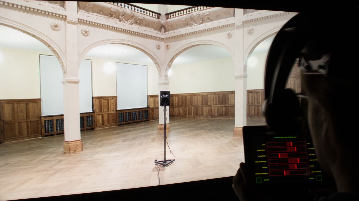 Room with wooden floor and a gallery on columns. On the right in the picture, the head of a test subject from behind.