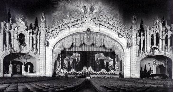 Paradise Theater in Chicago (1918) Zu sehen ist der prunkvolle Saal des Paradise Theaters in Chicago im Jahr 1918, ausgestattet mit hunderten Sitzplätzen. Im Zentrum der Bühne befindet sich der weiße Spieltisch der fünffach manualigen Wurlitzer-Orgel. Auf der linken Seite sind weitere Elemente der Orgelanlage zu sehen z.B. die Pfeifen.