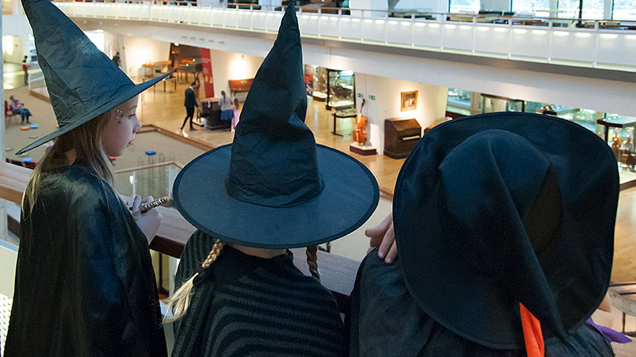 Drei als Hexen verkleidete Kinder schauen in den Ausstellungsraum des Musikinstrumenten-Museums